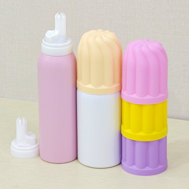 Three aerosol cans for mousse and foam: a pink can with a white foam nozzle, a cream can with a beige petal-shaped cap, and a two-tone yellow and purple can with a ribbed foam cap